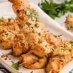 Single skewer being lifted from a serving plate, with extra skewers blurred in the background.