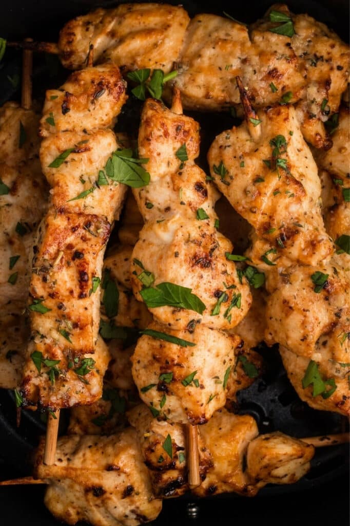 Close-up inside the air fryer basket focusing on several skewers with visible seasoning and fresh herbs.