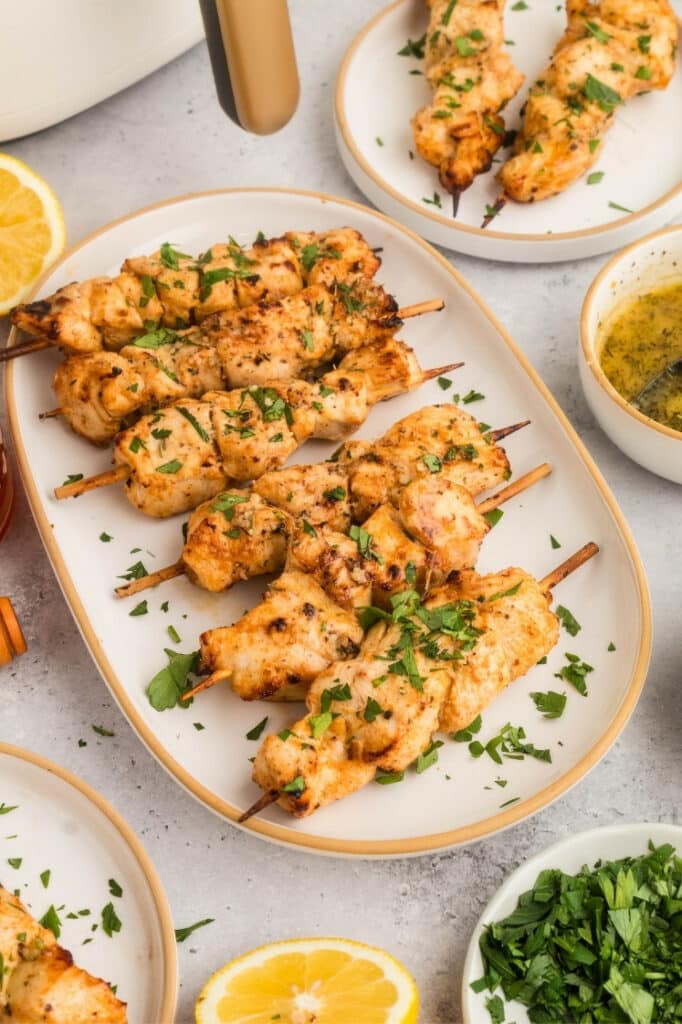 Overhead shot of chicken skewers inside the air fryer basket, surrounded by lemon, herbs, and small prep bowls.