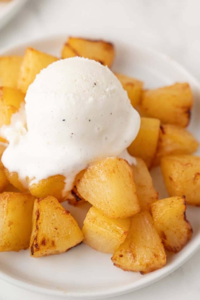Close-up of air-fried pineapple topped with a scoop of vanilla ice cream, beginning to melt over the warm fruit.