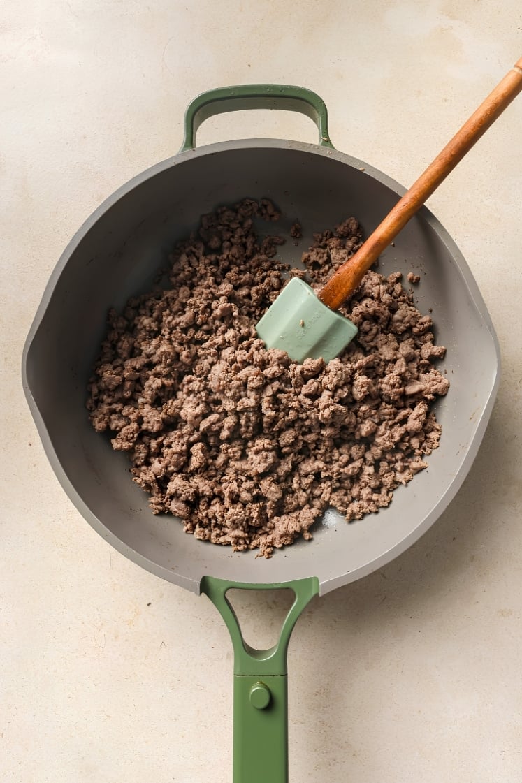 Overhead image of browned ground beef cooking in a skillet with a spatula resting inside the pan.