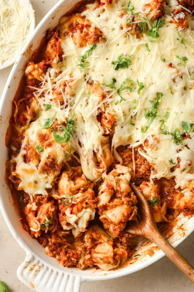 Close view of baked tortellini casserole with melted cheese pulled back to reveal the saucy layers underneath.