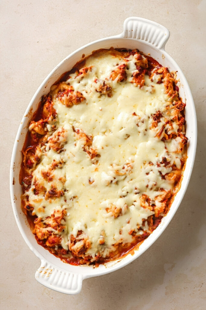 Finished baked tortellini casserole with melted golden cheese across the top in a white baking dish.