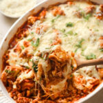 Partially served tortellini casserole showing the meat sauce, melted cheese, and wooden spoon after scooping.