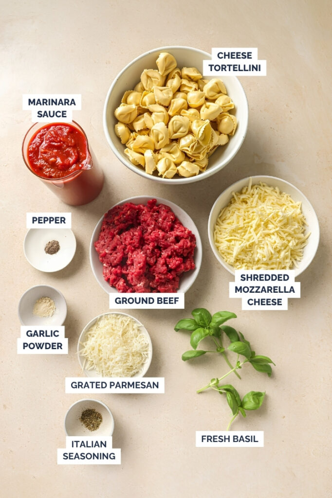 Ingredients for baked tortellini with meat sauce including cheese tortellini, ground beef, marinara sauce, mozzarella, Parmesan, garlic powder, Italian seasoning, pepper, and fresh basil.