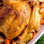 Close-up view of the crispy, glistening golden-brown skin of a roasted whole chicken inside a white baking dish surrounded by carrots and potatoes.