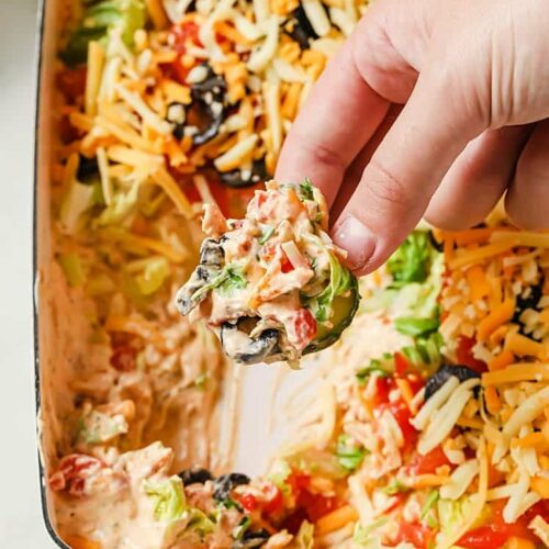 Taco dip with cream cheese topped with lettuce, tomatoes, olives and cheese