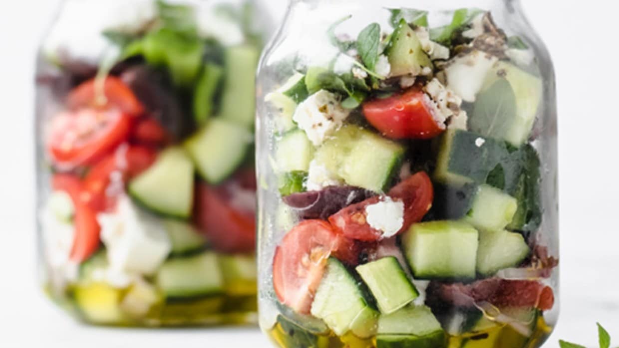 Two jars of layered greek salad on a marble counter.