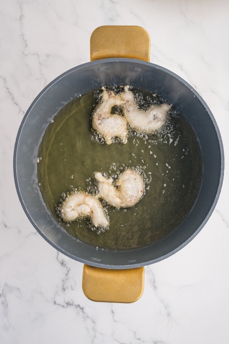 Battered shrimp frying in hot oil in a large pot.