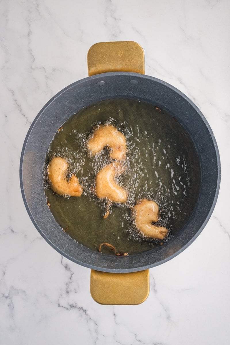Golden fried shrimp floating in hot oil in a large pot.