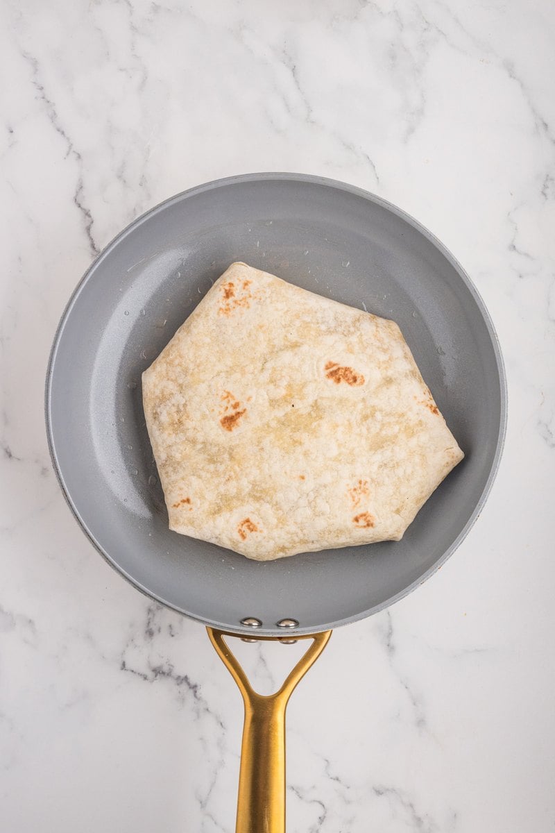 Folded breakfast crunch wrap placed seam side down in a gray skillet.
