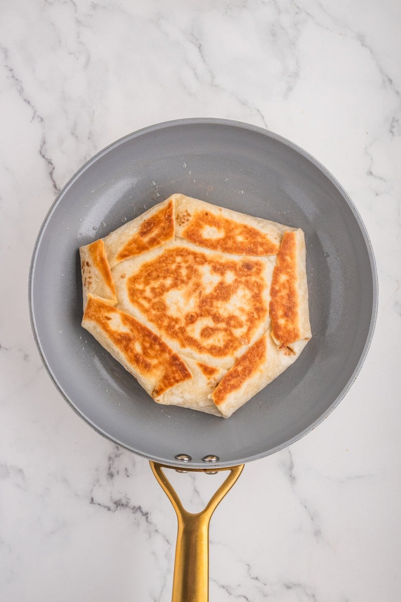 Breakfast crunch wrap flipped in the skillet showing a golden brown seared side.
