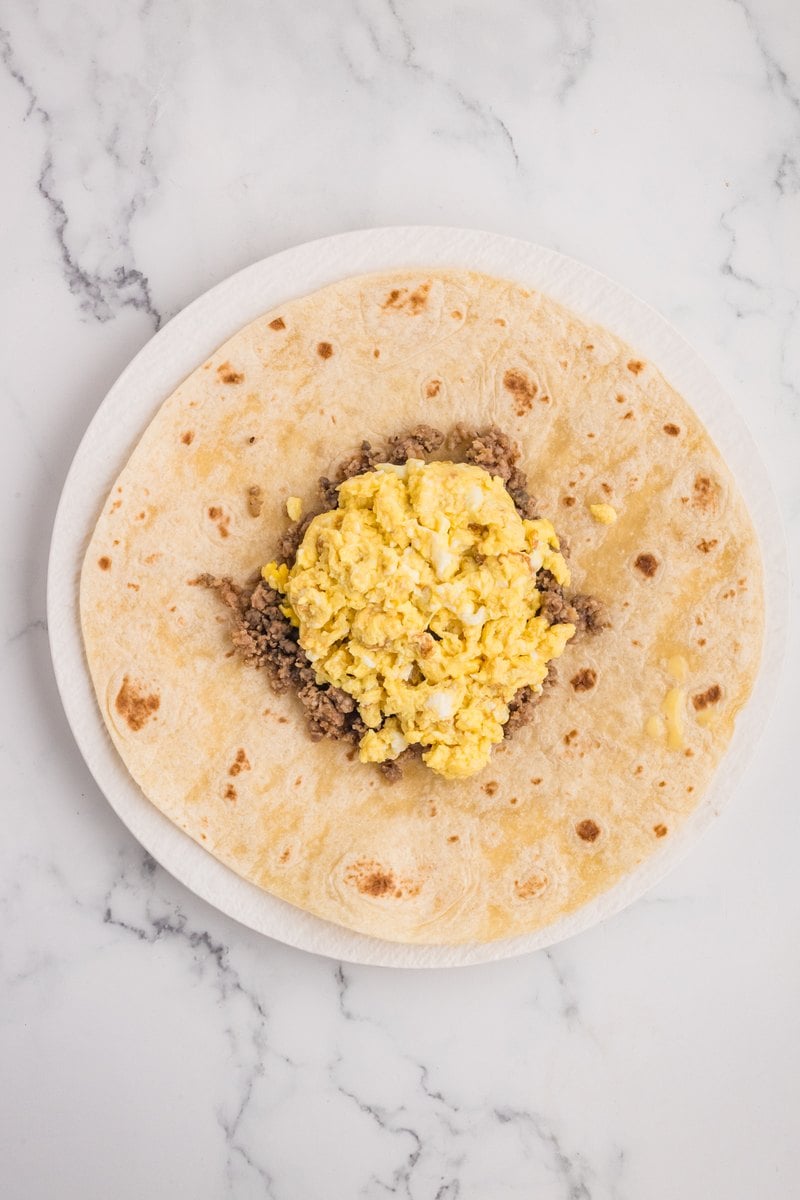 Scrambled eggs added on top of the sausage in the center of the tortilla.