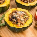 Roasted acorn squash half filled with sausage, apple, cranberry, and pecan stuffing and topped with melted Parmesan on a wooden board.