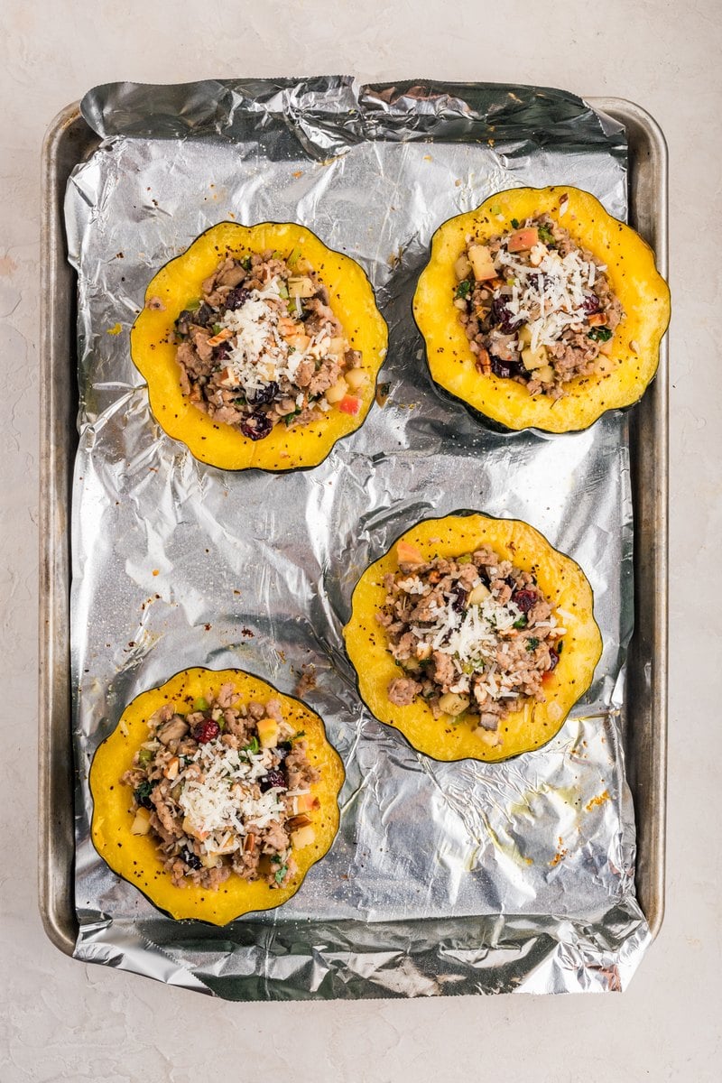 Stuffed acorn squash halves sprinkled with extra Parmesan before the final bake.