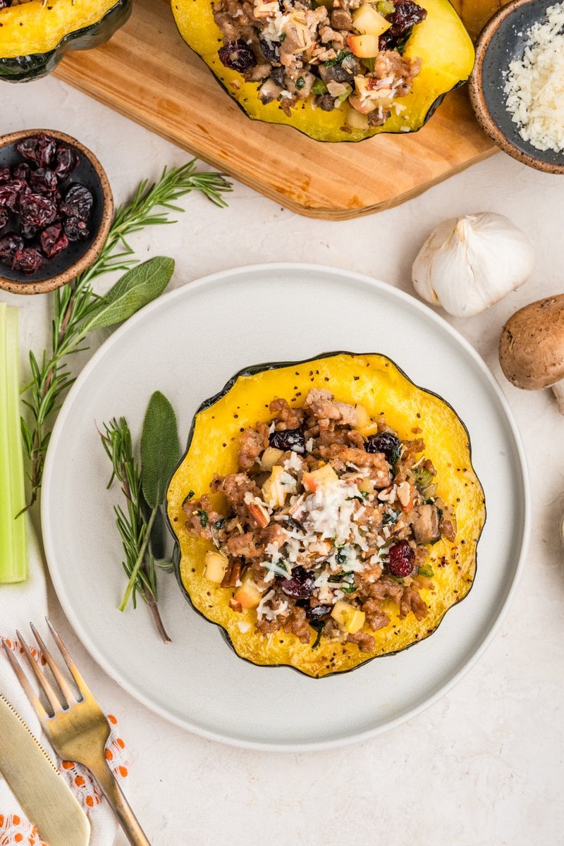 Finished stuffed acorn squash half on a white plate with fresh sage and a fork beside it.