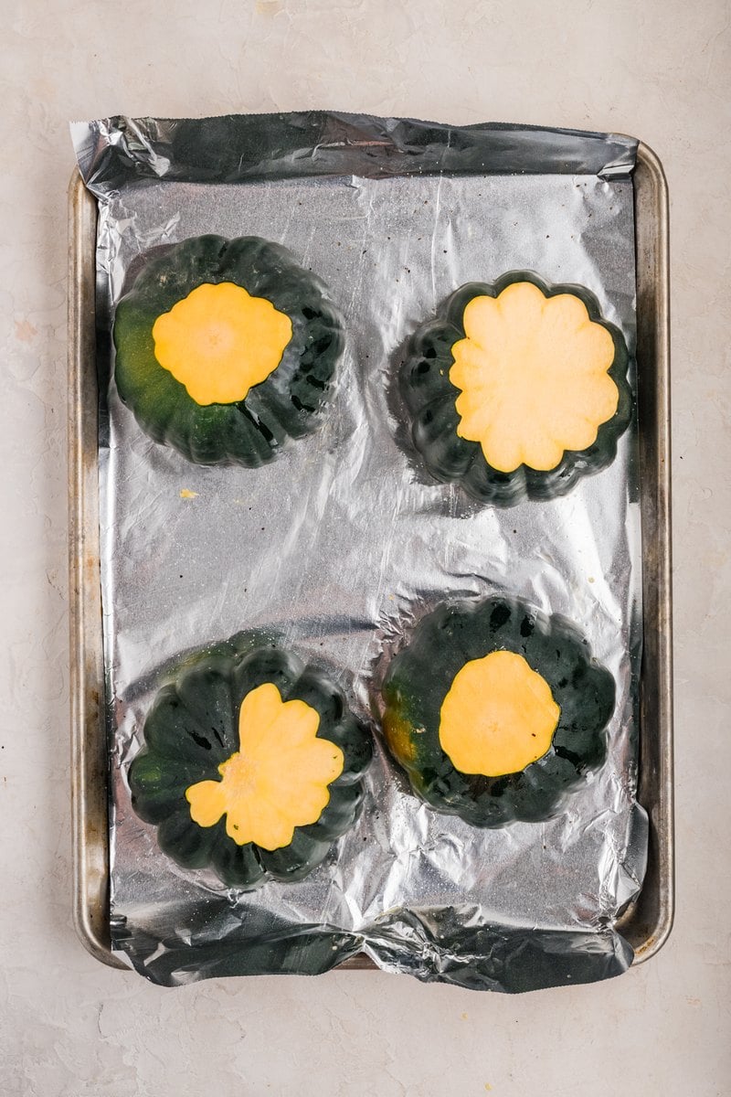 Seasoned acorn squash halves placed cut side down on the foil-lined baking sheet ready to roast.