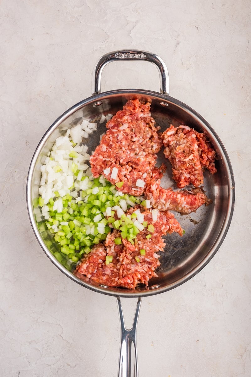 Raw Italian sausage, diced celery, and diced onion in a stainless skillet.