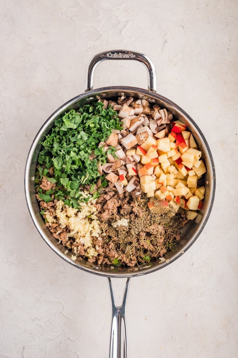 Chopped mushrooms, diced apple, kale, garlic, and dried herbs added to the browned sausage in the skillet.